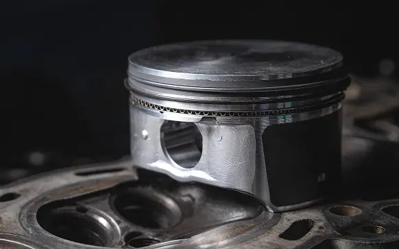 A close-up shot of a metallic engine piston resting on a matching metal engine block against a dark, moody background.