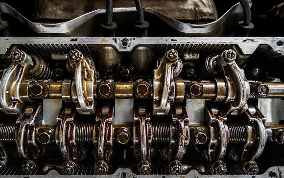 Close-up of an engine's camshaft and valve components, showing metallic silver and bronze parts with dark oil and grime.