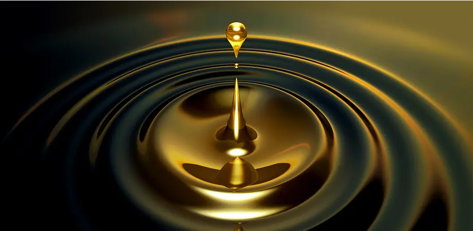 Gold droplet falling into oil creating concentric ripples on a dark background